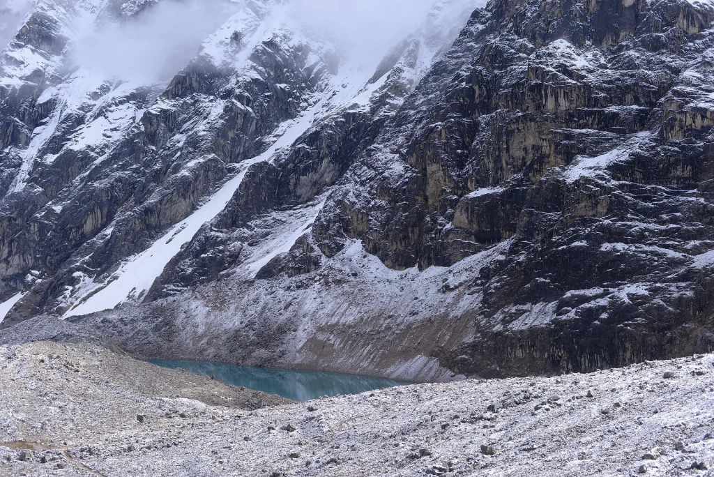 Laguna turquesa al pie de paredes nevadas cerca del paso Inca Chiriaska, en la ruta Salkantay